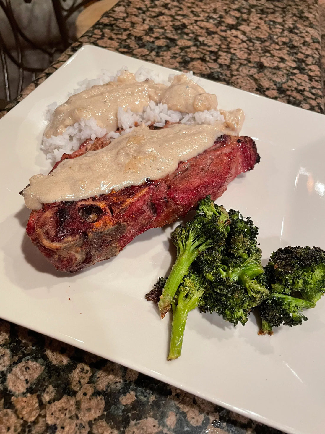 Cooked meat with creamy gravy, white rice, and roasted broccoli on a white plate.