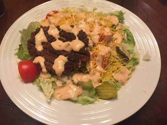 Low-carb "Big Mac" salad with hamburger patty, special sauce, cheddar, tomatoes, and pickles on a bed of lettuce.